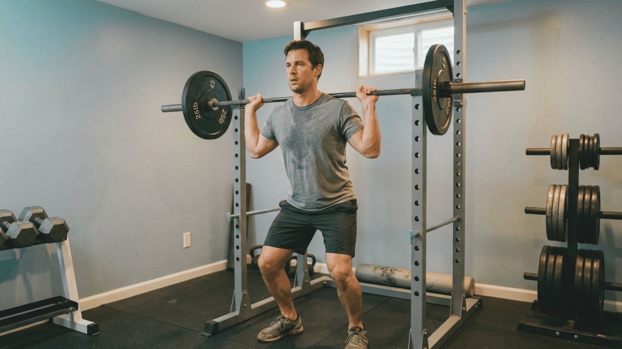man performing a barbell squat in a home gym as part of a strength training routine