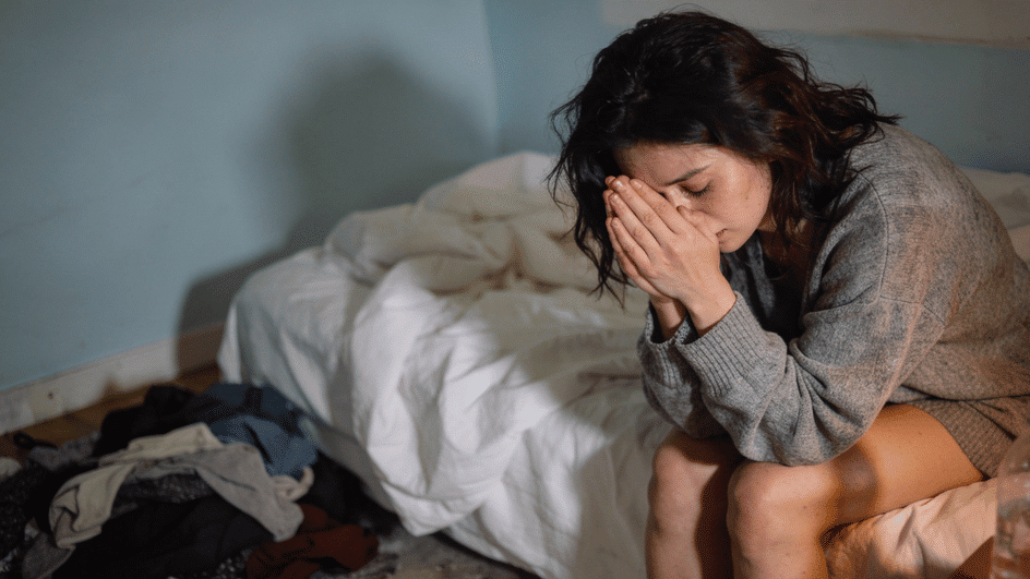 Woman sitting on a bed experiencing emotional distress associated with BPD.