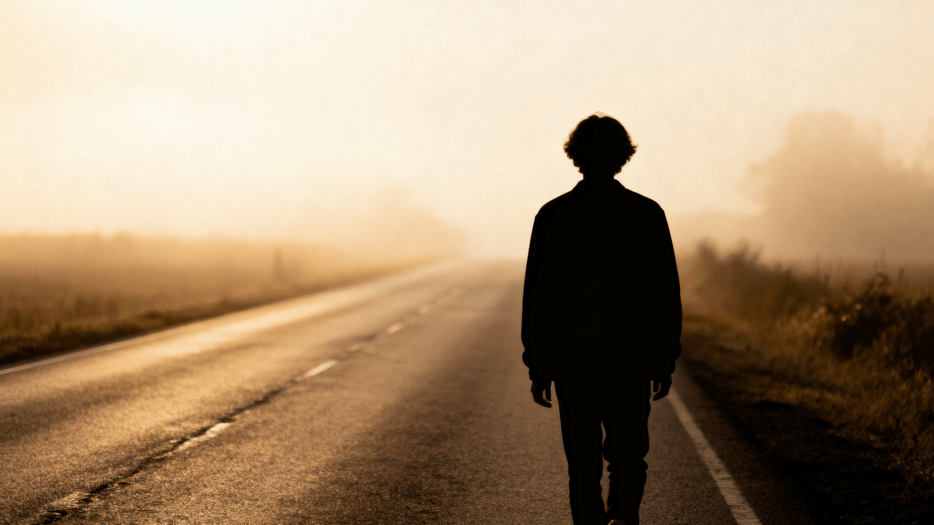 silhouette of a person walking alone down a long empty road at golden hour in shallow depth of field