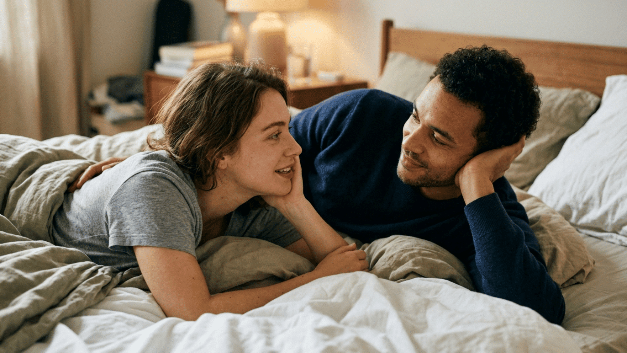 couple lying on a bed having an intimate conversation while smiling and listening closely to each other
