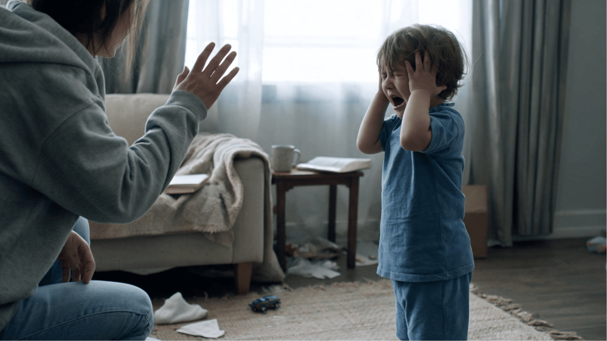child covering ears and crying while a parent kneels nearby using a calming gesture
