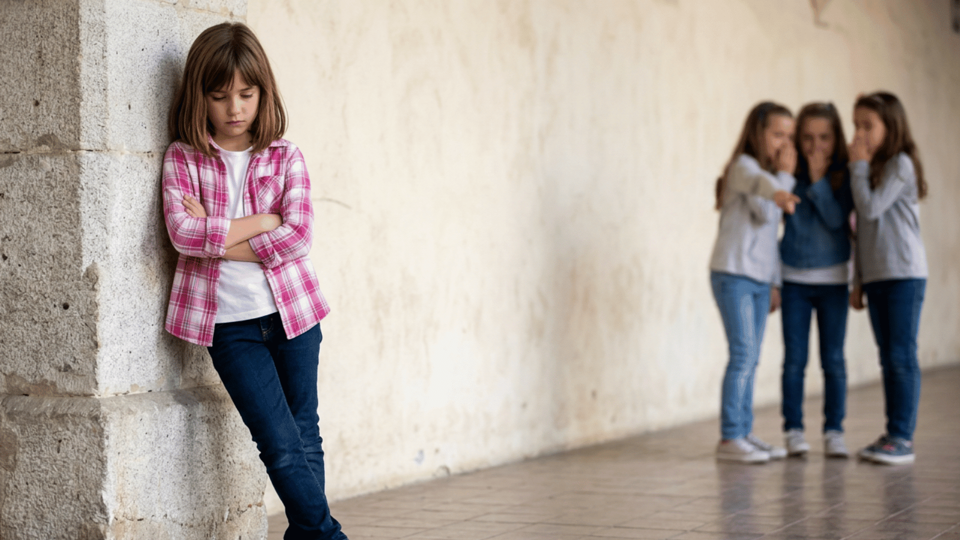 a sad girl stands alone against a wall as three classmates whisper and point at her in the background