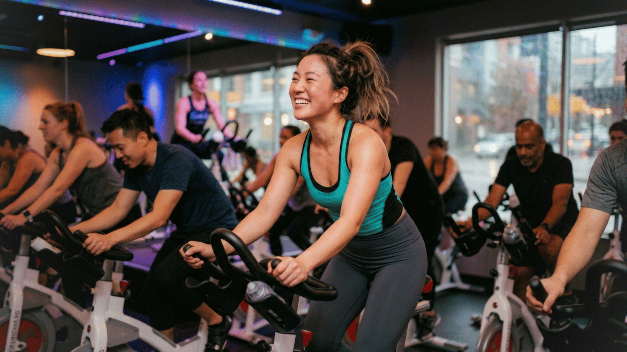 smiling woman enjoying an energetic indoor cycling class with others in a modern fitness studio