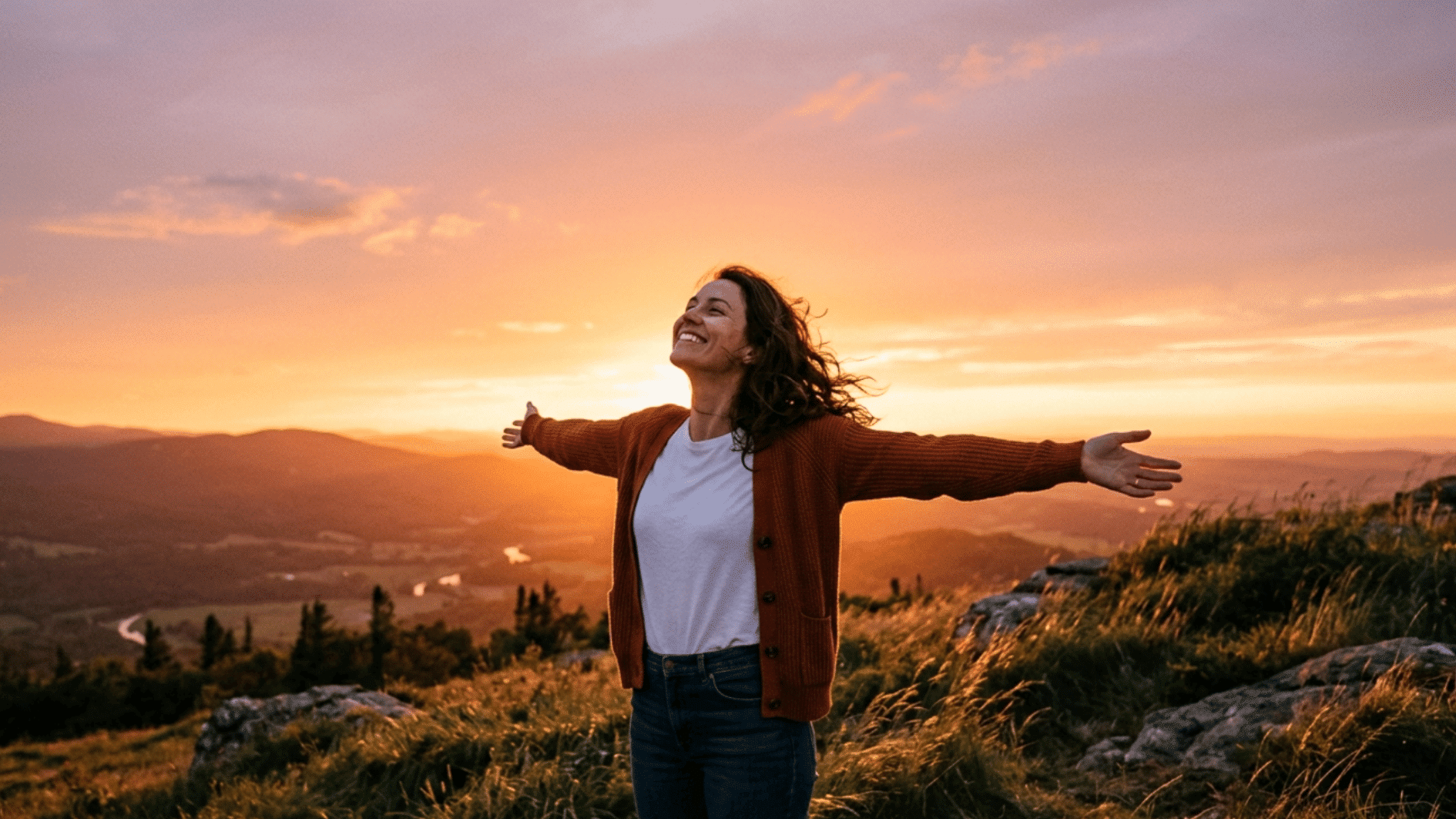 woman standing on a mountain ridge at sunset with arms outstretched, embracing living life to the fullest