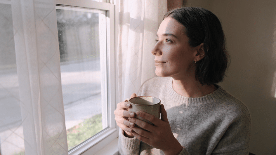 a woman gazing out a window with a calm expression, representing stillness and healing during trauma recovery